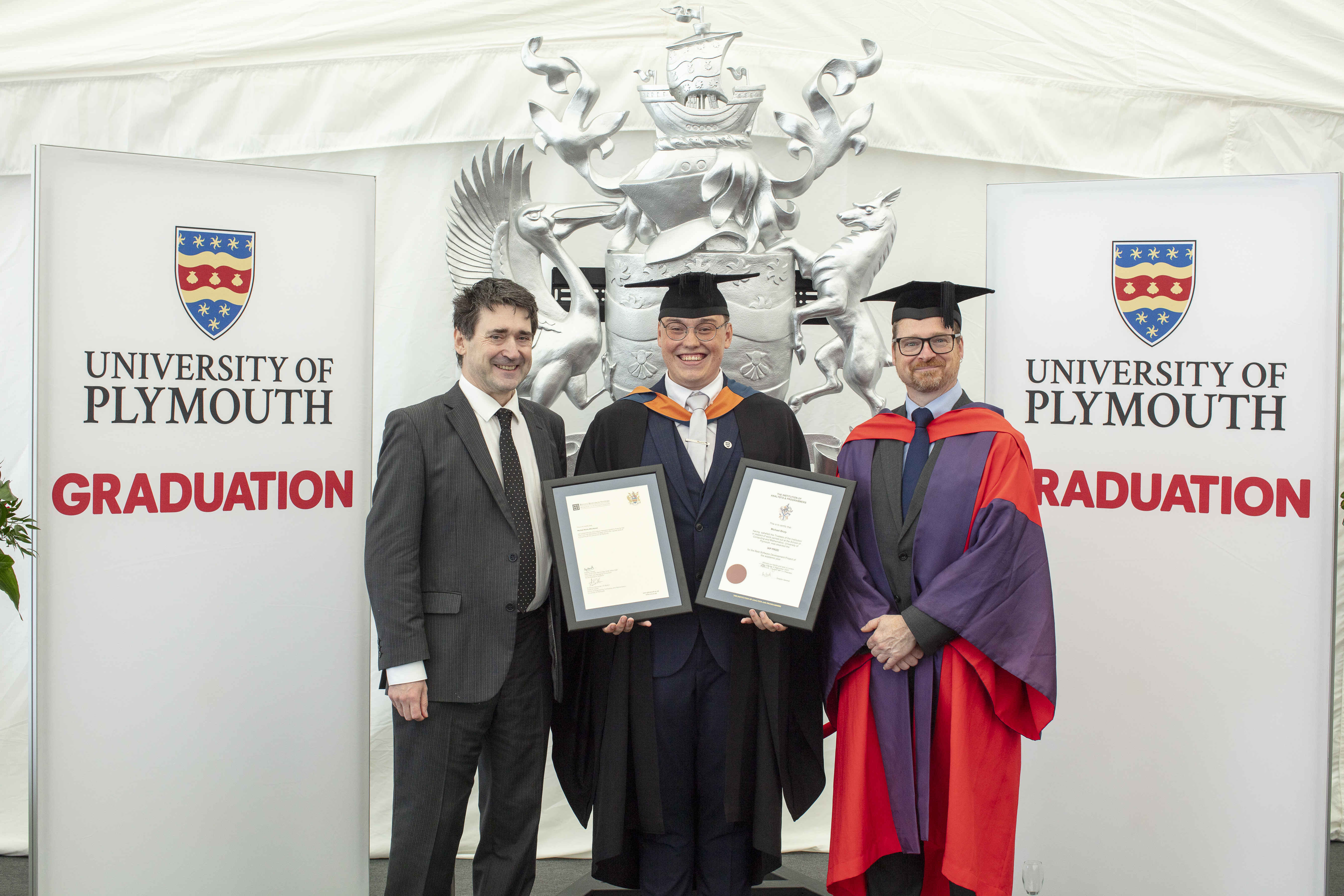 Michael Bruty holding both the Revell Research Systems Prize and the Institution of Analysts and Programmers Prize, flanked by Alastair Revell (left) and Professor Alexander Belton (right).
